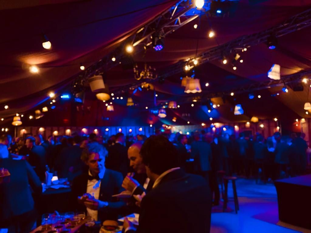 Druk bedrijfsfeest in blauw en warm licht met schemerlampen boven de gasten